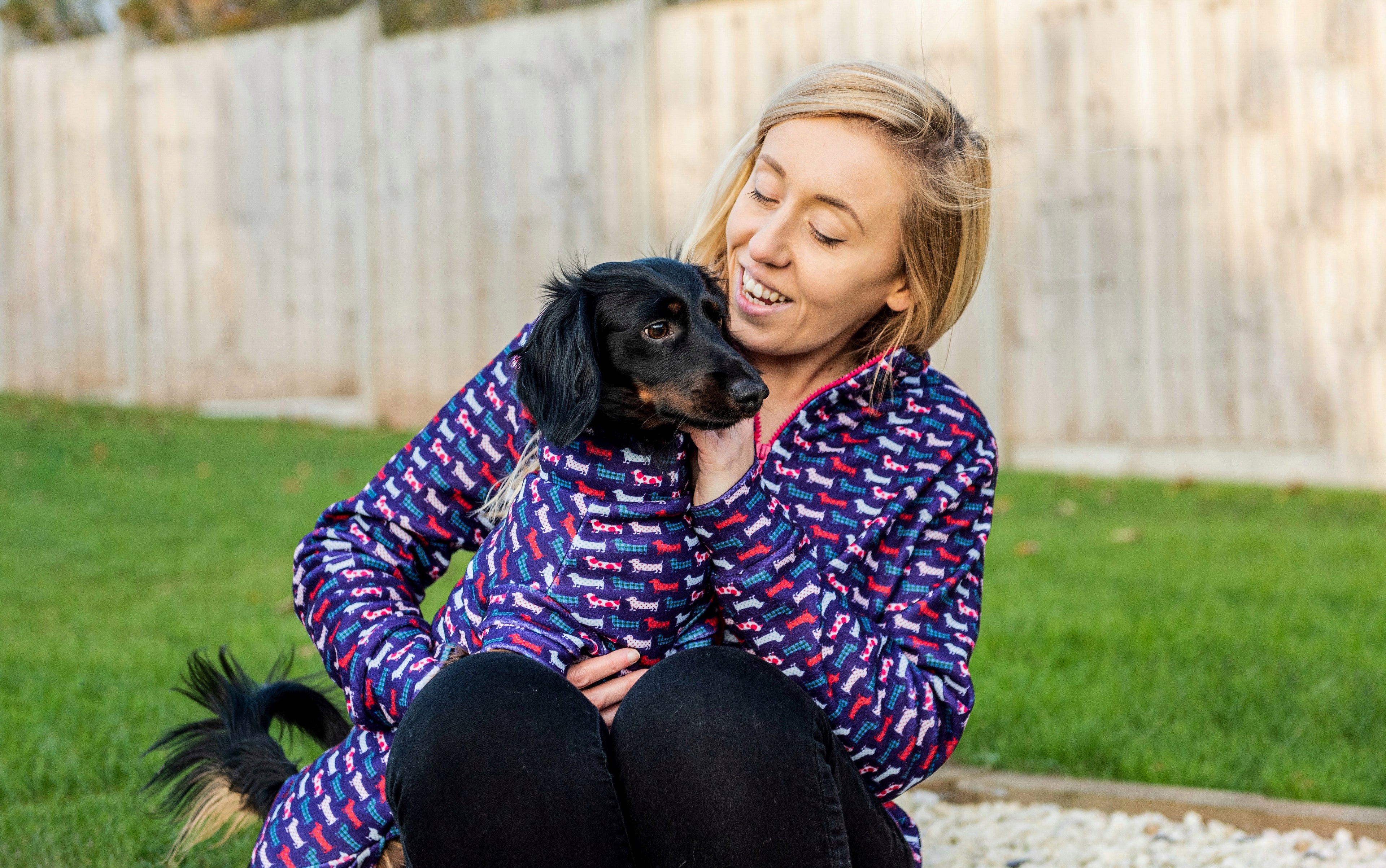 Blonde woman and her miniature dachshund wearing matching jumpers with a dachshund print design.