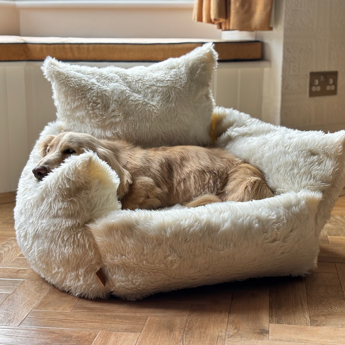 Dog lying on a fluffy white pet bed in a cozy room with wooden flooring.