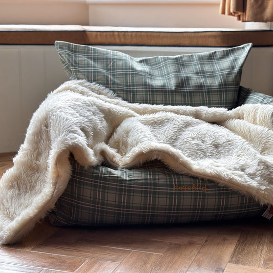 Dog bed with plaid pattern and white blanket on a wooden floor