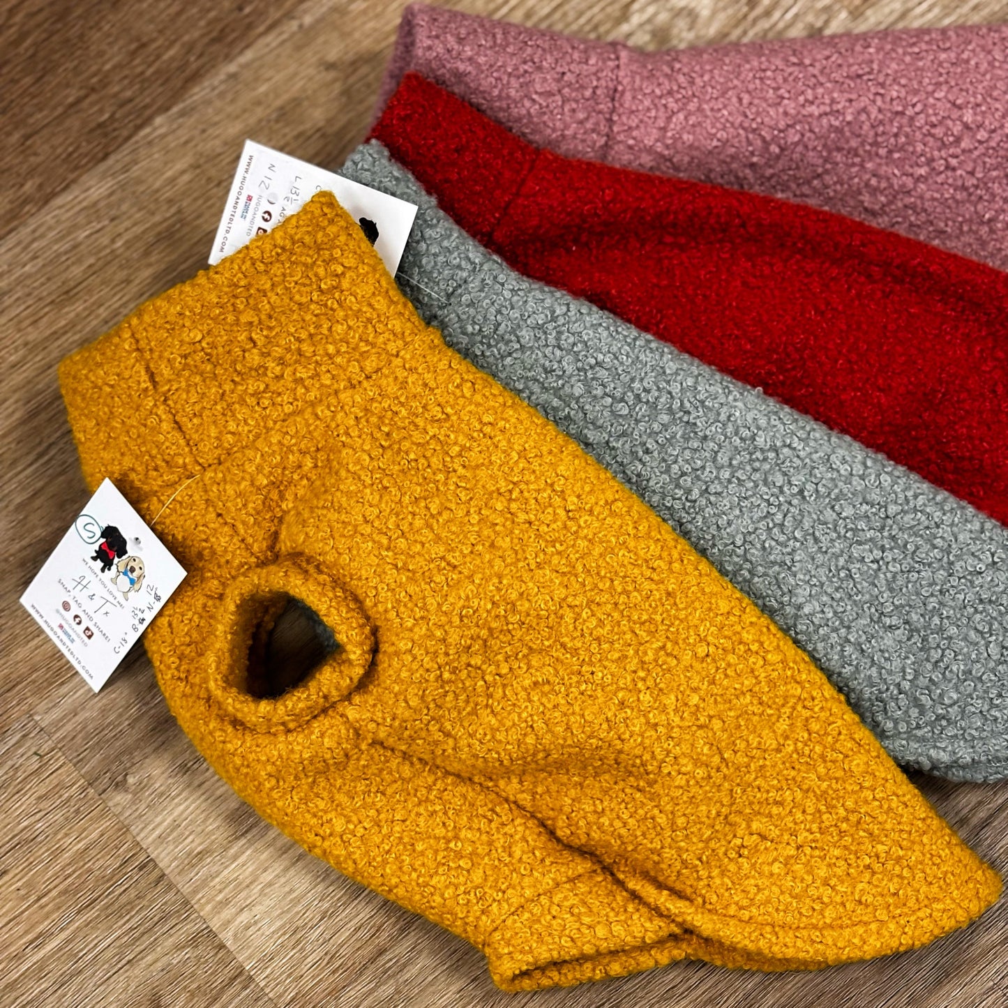 Four folded fabric samples in yellow, red, gray, and pink on a wooden surface with a visible brand tag.