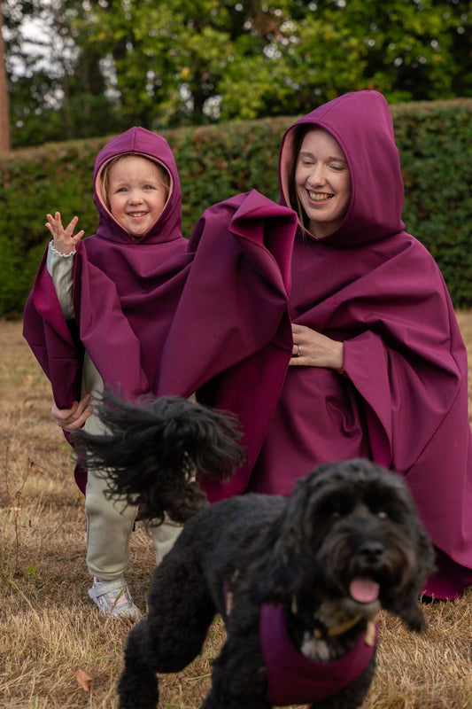 Two people in plum rain ponchos with a black dog