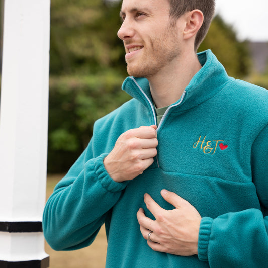 Man wearing a teal fleece with a logo, standing outdoors.