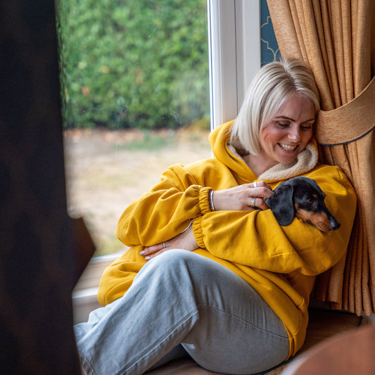 Woman in a yellow hoodie holding a small dog by a window