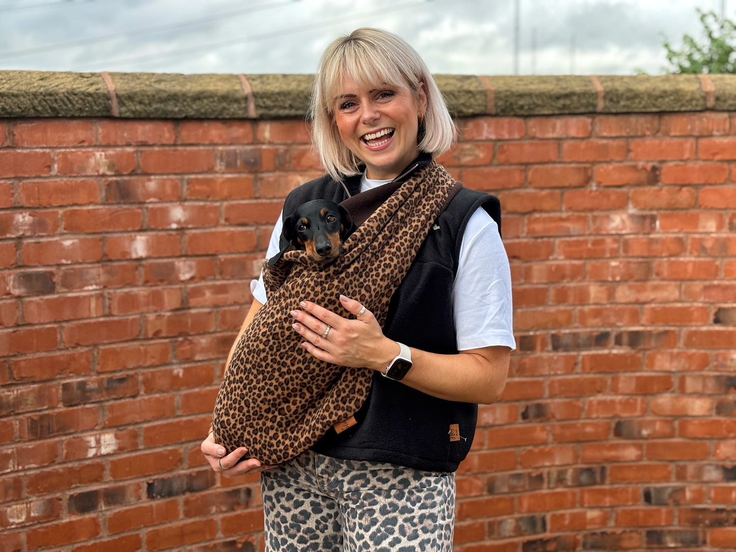 Woman by a brick wall wearing a leopard print fleece dog sling