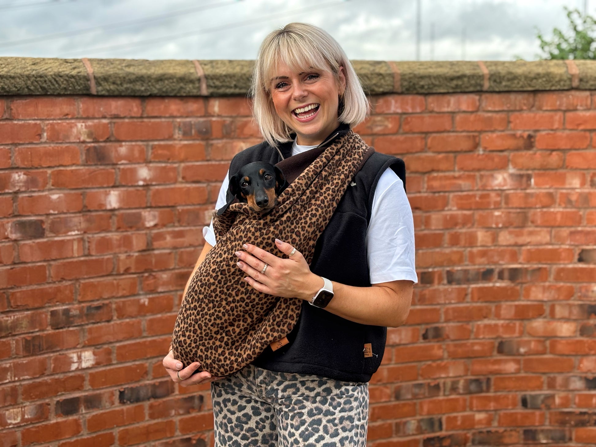 Woman by a brick wall wearing a leopard print fleece dog sling