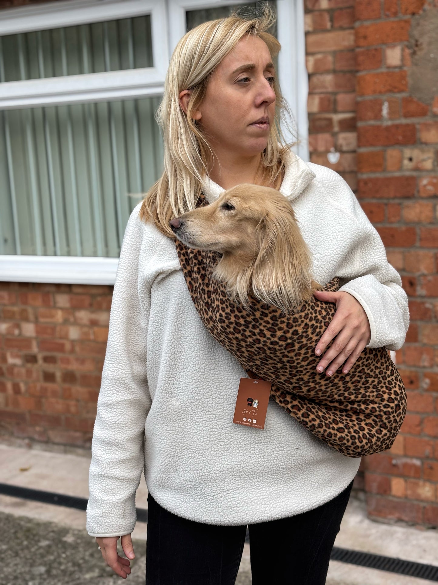 Woman outdoors carrying a dog in a leopard print fleece sling