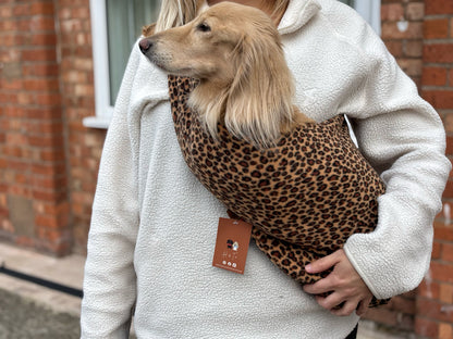 Dog peeking out of a leopard print fleece sling worn with a grey hoodie