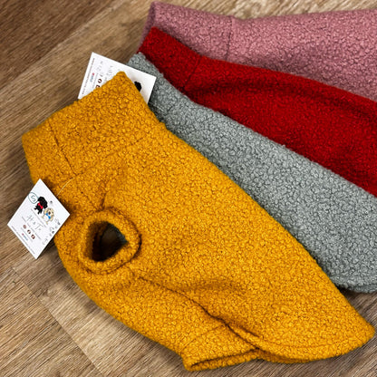 Four folded fabric samples in yellow, red, gray, and pink on a wooden surface with a visible brand tag.