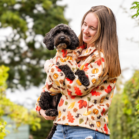 Woman holding a black dog in an autumn-themed sweater with a blurred garden background