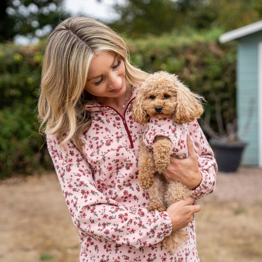 Woman holding a small dog in a floral outfit outdoors with a shed in the background