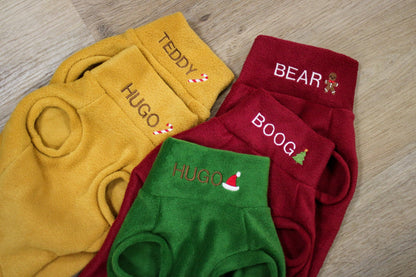 Mustard, red and green Christmas fleece dog jumpers laid flat with embroidered names